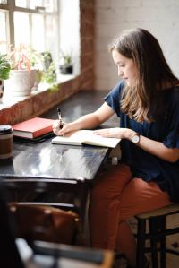 person wit long hair sitting ata desk writing in a journal